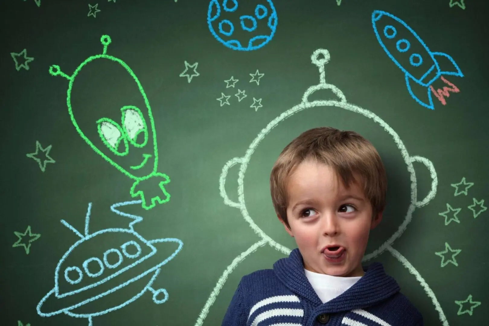 A boy in front of a chalkboard with drawings on it.